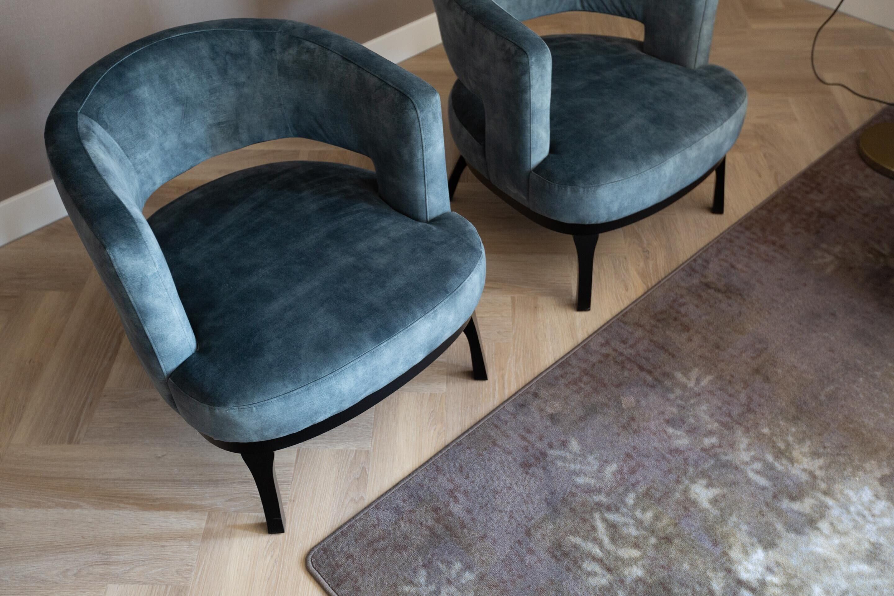 Two modern armchairs with a dark fabric, wooden legs, and a light wooden floor.