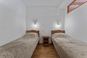 A small, clean room with two single beds, a wooden nightstand between them, and a small table.