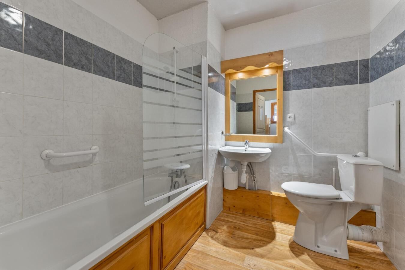 A bathroom with a glass shower enclosure, a sink, a toilet, and wooden flooring.