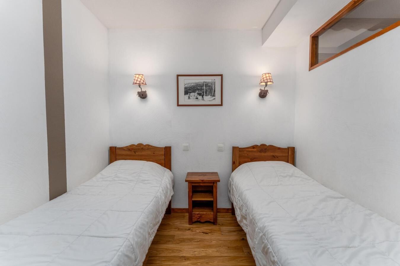 Ein kleines, sauberes Zimmer mit zwei Einzelbetten, einem Nachttisch und einem gerahmten Bild an der Wand.