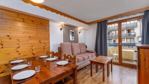 Un coin repas avec une table en bois dressée pour quatre personnes, un canapé et un balcon offrant une vue sur un immeuble.
