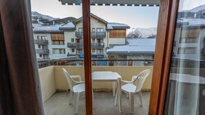 Un balcon avec une table et des chaises, donnant sur une montagne enneigée et des bâtiments.