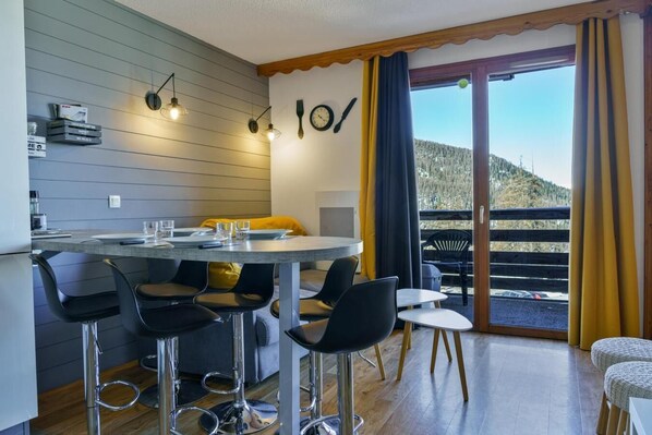 A modern kitchen with a dining area, bar stools, and a view of a mountain.