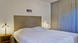 A neatly made bed with a white duvet, a wooden nightstand with a lamp, and a wooden headboard.