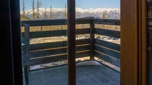 A balcony with a view of snow-covered mountains and a parking area.