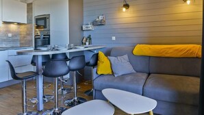 A modern living room with a grey sofa, a yellow throw, and a dining area with bar stools.