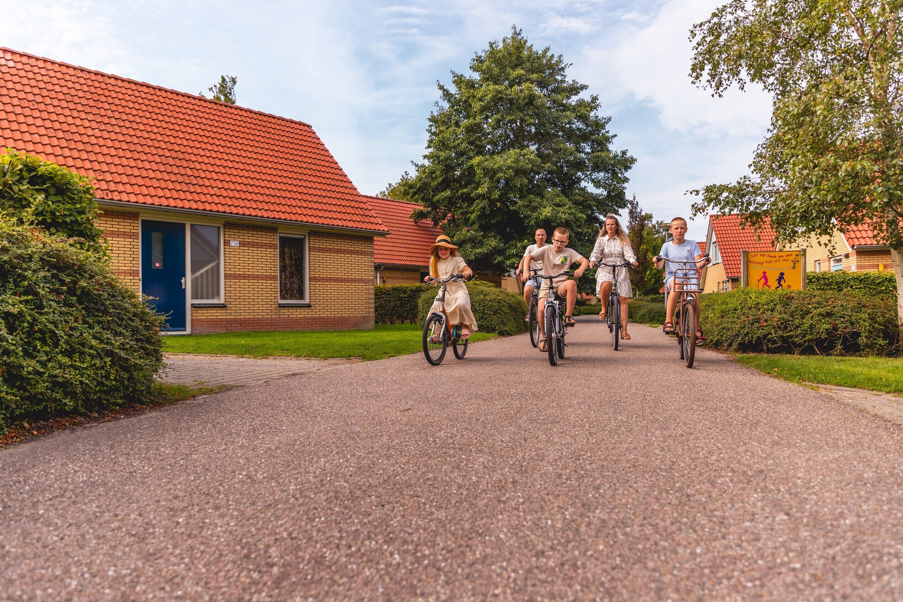 A residential street with a red-tiled roof house, a blue door, and a paved driveway.