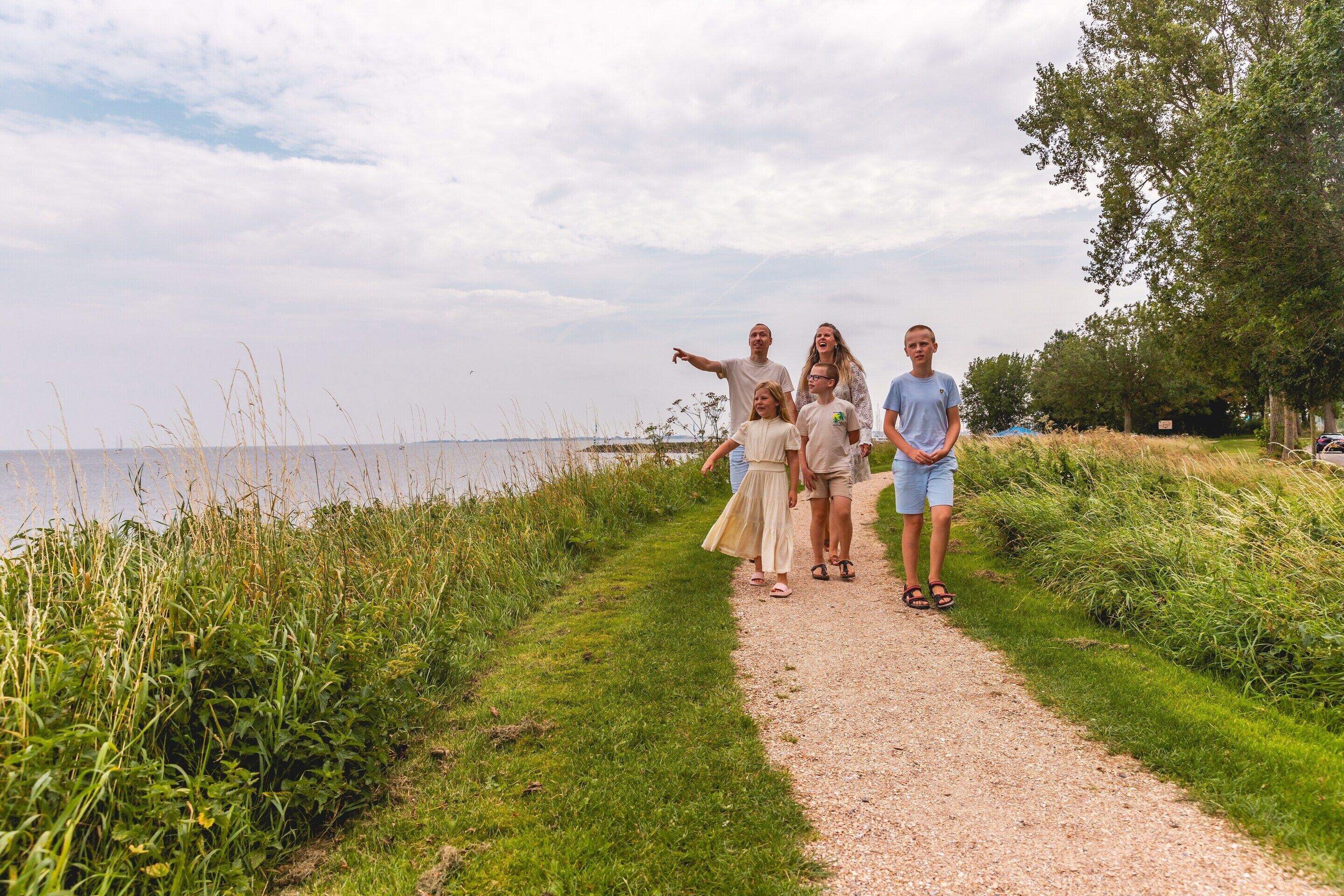 En grupp människor promenerar på en grusväg intill ett vattendrag, omgivna av grönska.