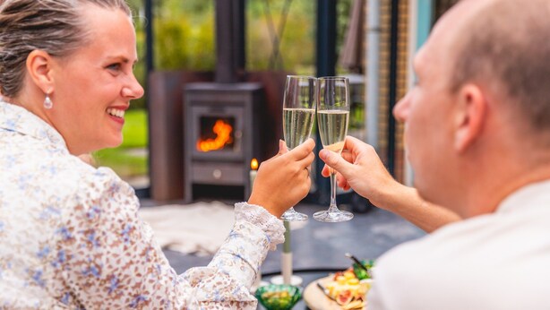Two people toasting with champagne glasses at an outdoor table with a wood-burning stove in the background. - Scenic Villa in Andijk Near Lake (Andijk)