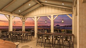 Enjoy dining with a view of the water from this outdoor dining area, featuring tables and chairs beneath pendant lights.