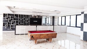 A modern living room with a pool table, a TV, and a geometric wall design. - Luxe Apartment with Rooftop Pool & Gym near the Airport. (Accra)