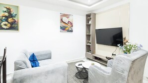 A modern living room with two grey armchairs, a coffee table, a flat-screen TV, and decorative wall art. - Luxe Apartment with Rooftop Pool & Gym near the Airport. (Accra)