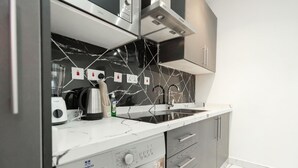 A modern kitchen with a built-in washing machine, a coffee maker, and a sink. - Luxe Apartment with Rooftop Pool & Gym near the Airport. (Accra)