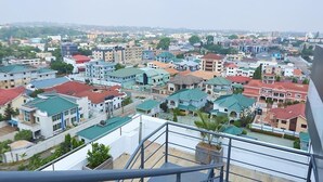 A residential area with various buildings, including multi-story apartment complexes and single-family homes, viewed from a balcony. - Luxe Apartment with Rooftop Pool & Gym near the Airport. (Accra)