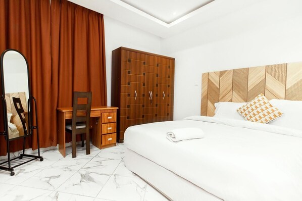Een hotelkamer met een bed, een houten kledingkast, een bureau met stoel, en een spiegel.