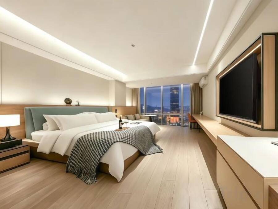 Quarto de hotel moderno com uma cama grande, mesas de cabeceira, escrivaninha e uma janela ampla com vista para a cidade.