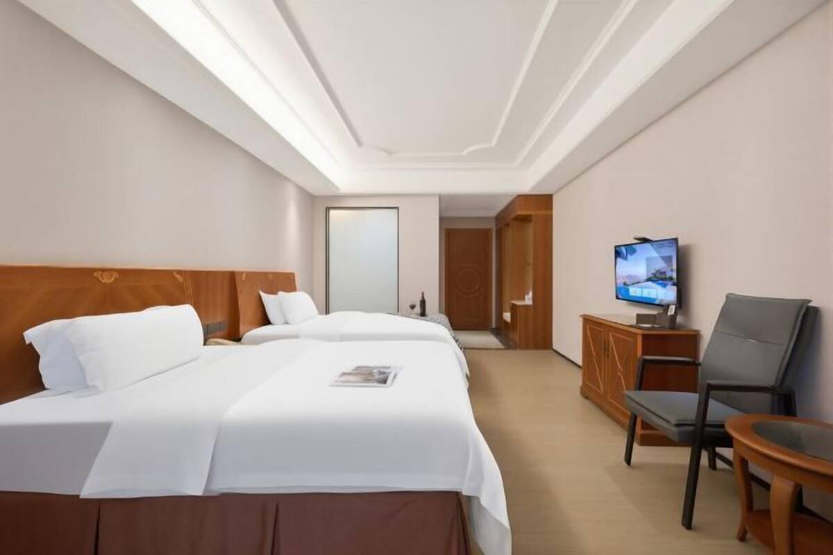 Hotellihuone, jossa on kaksi sänkyä, televisio, työpöytä ja tuoli.