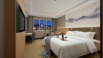 Habitación de hotel con cama, escritorio, silla, mesita y ventana con vista a la ciudad.