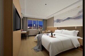 A hotel room with a bed, a desk, a chair, a small table, and a window with a city view.