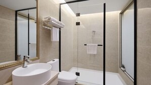 Un baño moderno con un espejo grande, un lavabo redondo, un inodoro y una zona de ducha con mampara de cristal.