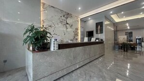 Una moderna zona de recepción con mostrador de mármol, una planta en maceta y una pantalla digital.