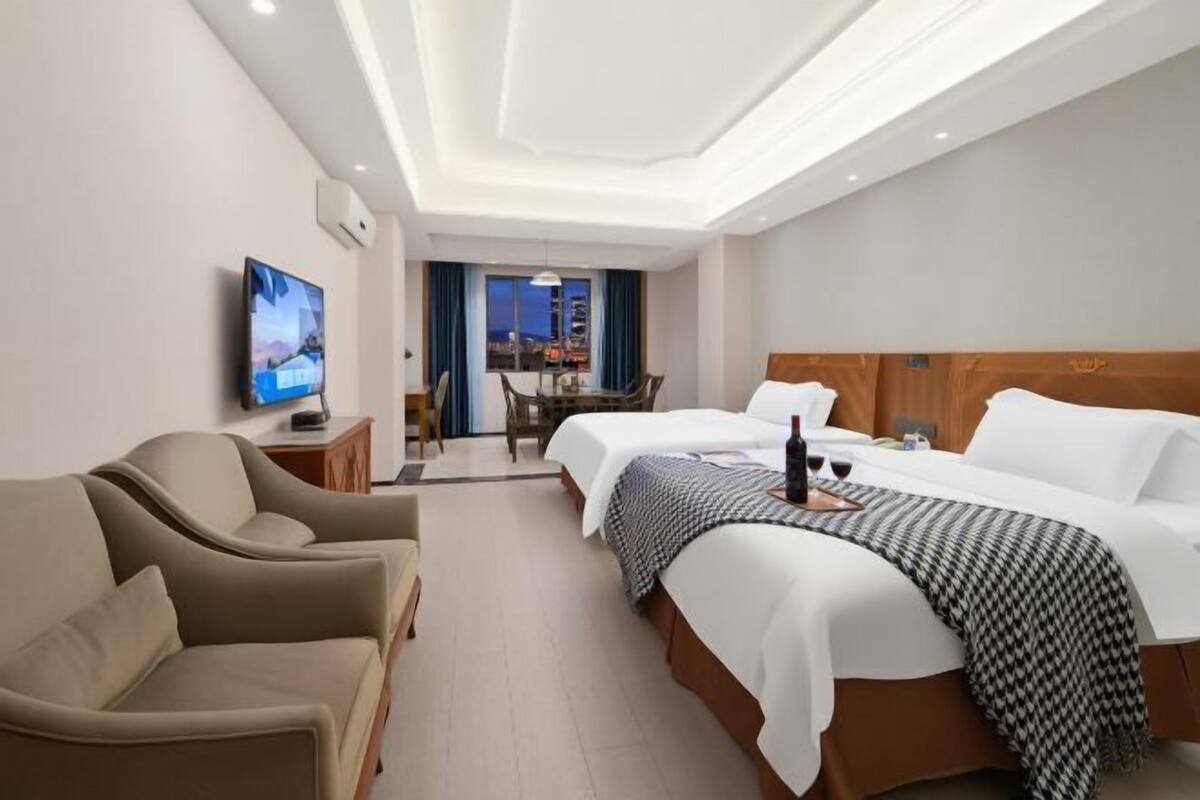 Hotellihuone, jossa on kaksi sänkyä, televisio, ruokailutila ja näkymä kaupunkiin.