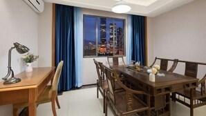 Un área de comedor con vistas a la ciudad, una mesa, sillas, una lámpara y un florero con flores.