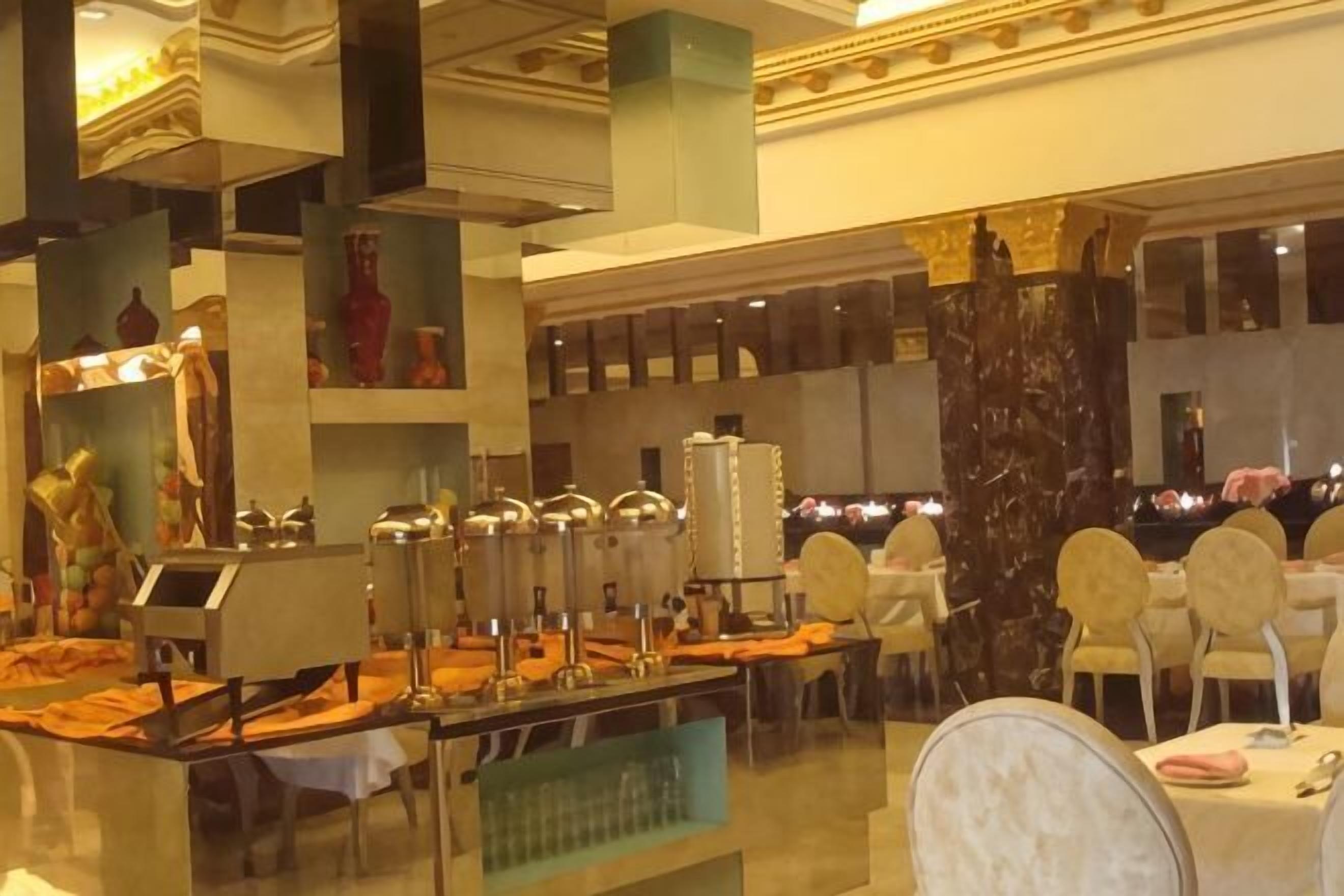 Un buffet avec plusieurs points de service, une colonne en marbre et un espace détente avec des tables et des chaises rondes.