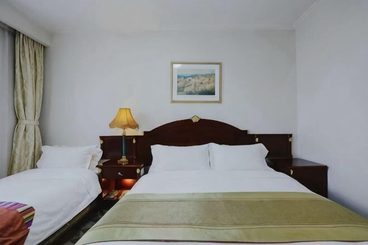 Habitació d'hotel amb un llit doble, dues taules de nit, una làmpada, un quadre a la paret i una finestra amb cortines.