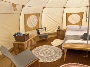 A cozy tent interior with a bed, a chair, a small table, and a round rug. - Beautiful Bell Tent Stay (Cowbridge)
