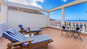 Un balcón con dos tumbonas, una mesa con sillas y vista al mar.
