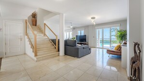 Amplia sala de estar con una escalera, un sofá gris, un televisor y un balcón con vistas.