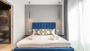 A modern bedroom with a large bed, a blue headboard, and a visible logo on the bed. - Saint Margaret Apartments (Cagliari)