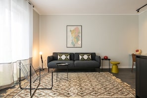 A modern living room with a patterned rug, a sofa with decorative pillows, a small round table, and a map on the wall.