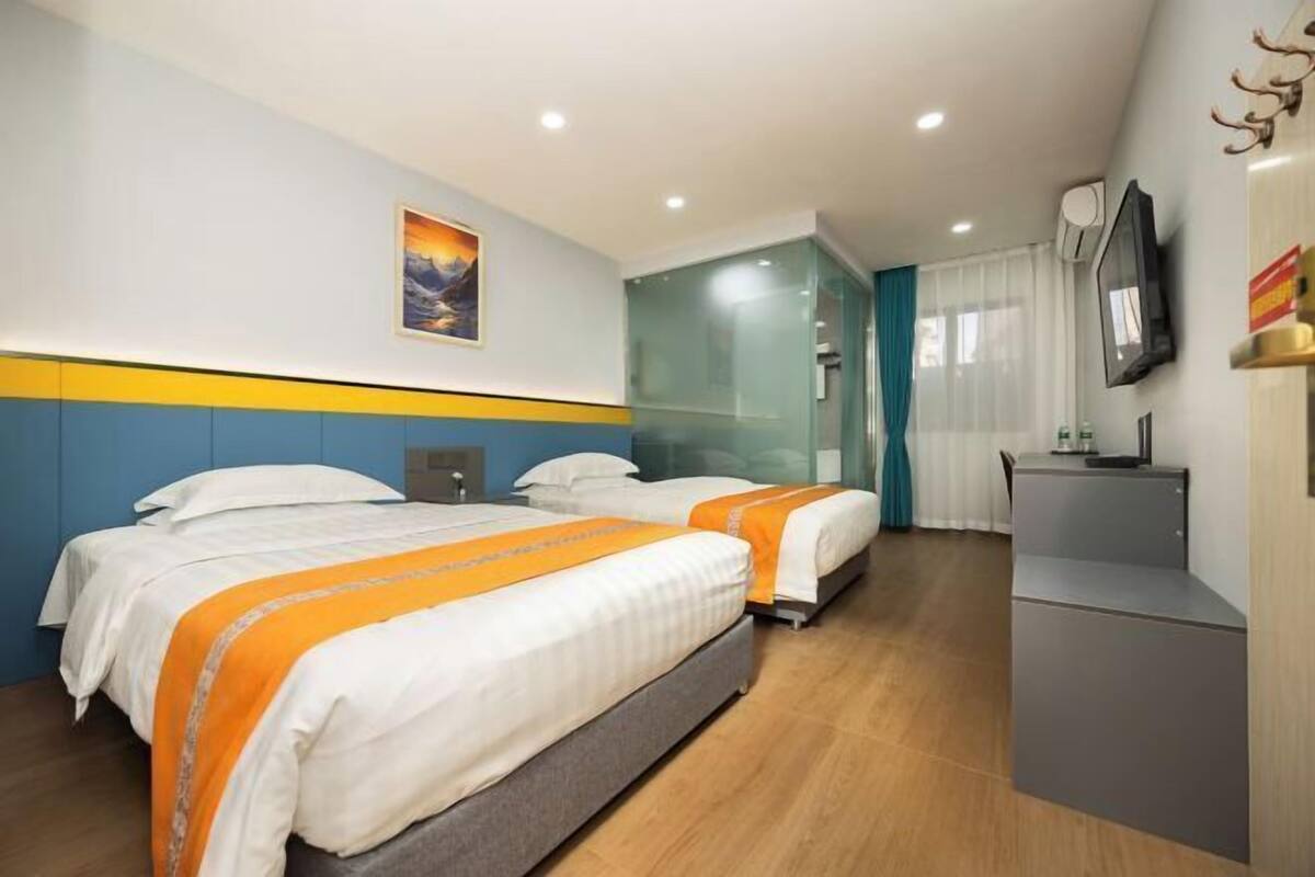 A hotel room with two beds, a desk, a TV, and a painting on the wall.