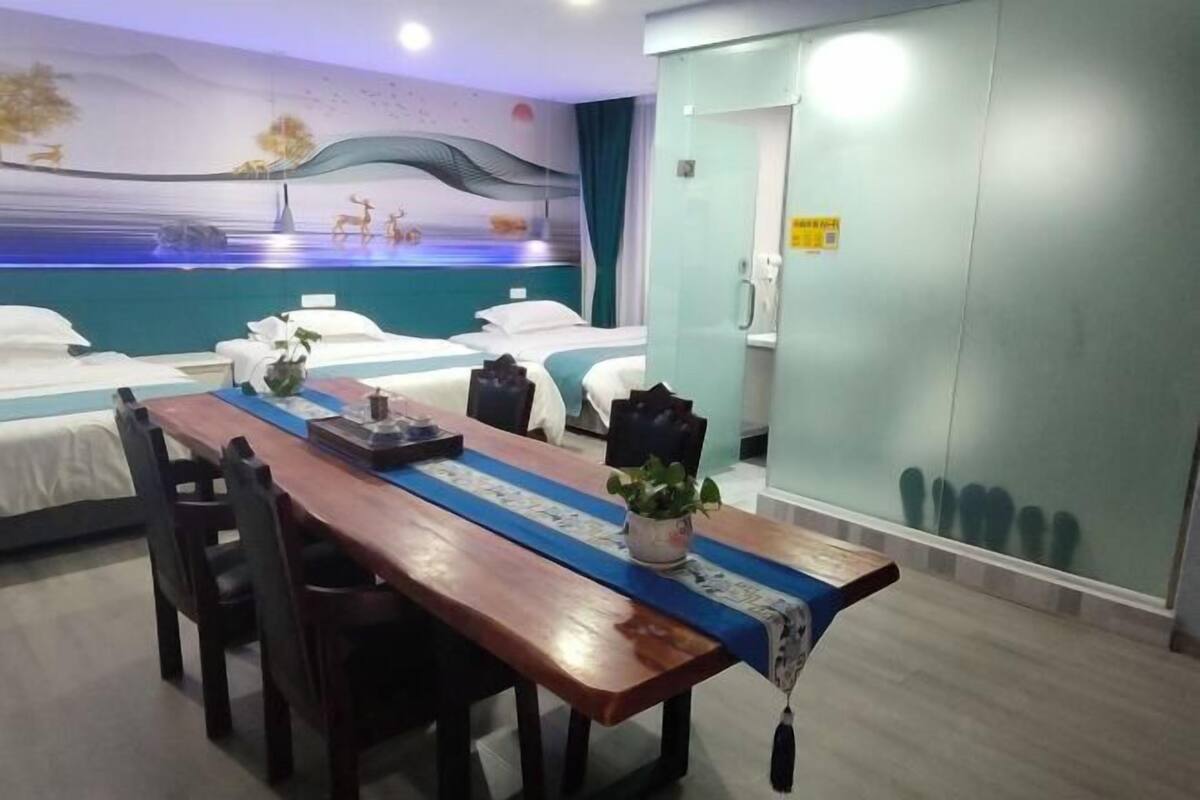 A hotel room with two beds, a wooden dining table, a mural on the wall, and a glass partition.