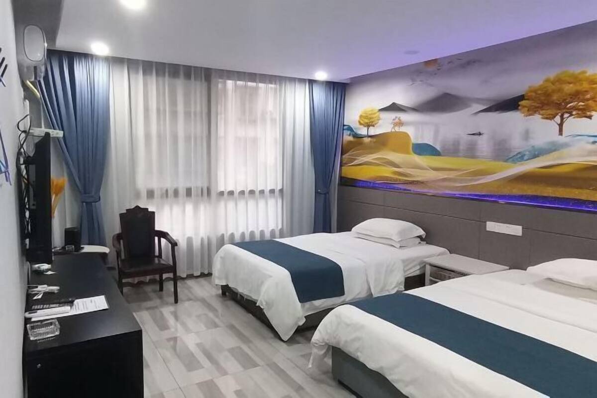 A hotel room with two beds, a desk, a chair, and a mural on the wall.