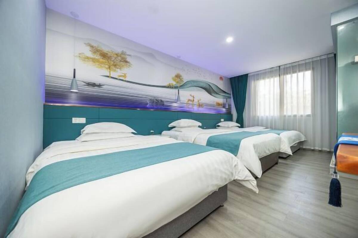 A hotel room with two beds, a mural on the wall, and a window with curtains.