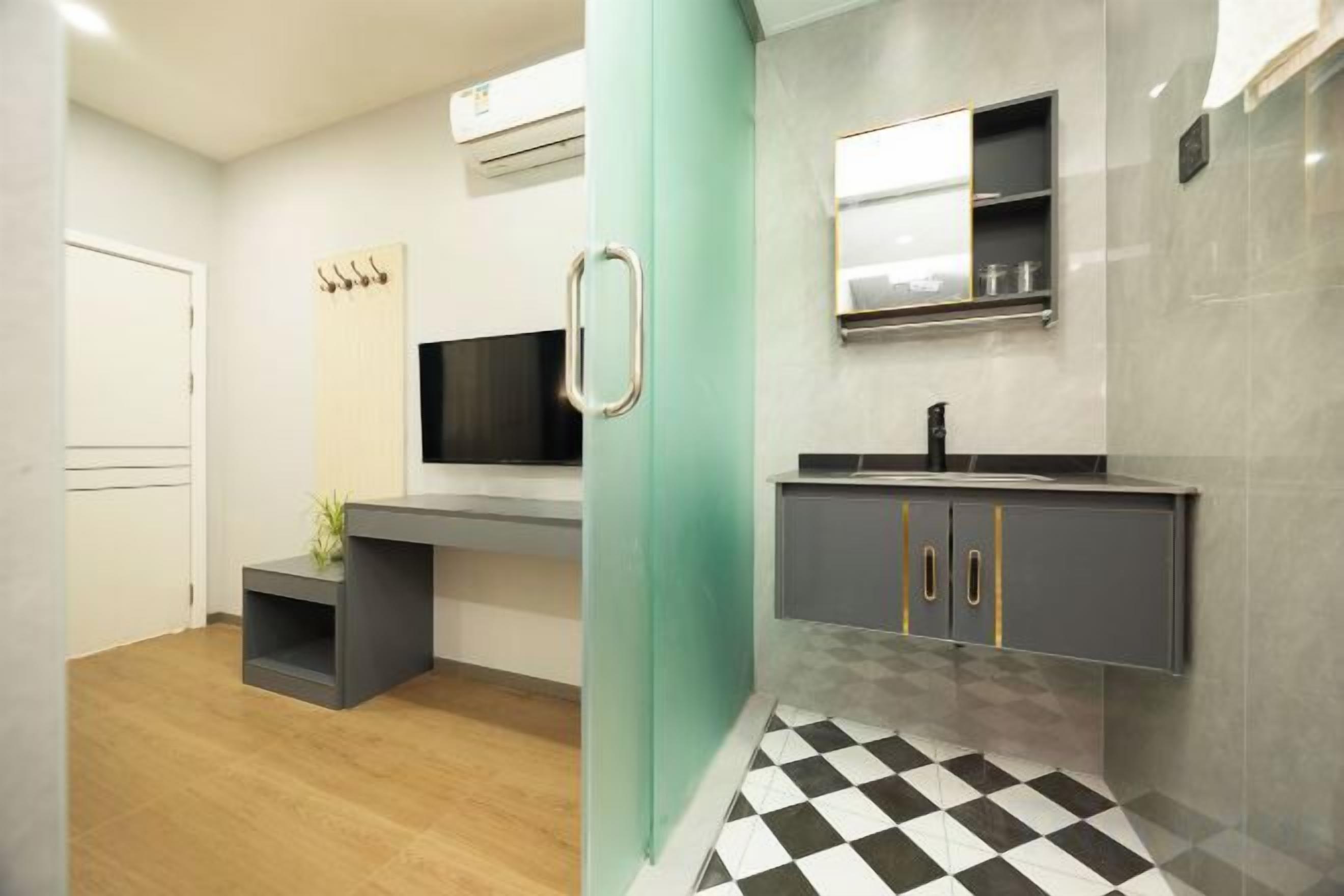 A modern bathroom with a black and white checkered floor, a grey vanity with a mirror, and a wall-mounted TV.