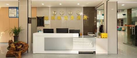 A reception area with a white reception desk, a plant, and a wooden sculpture.