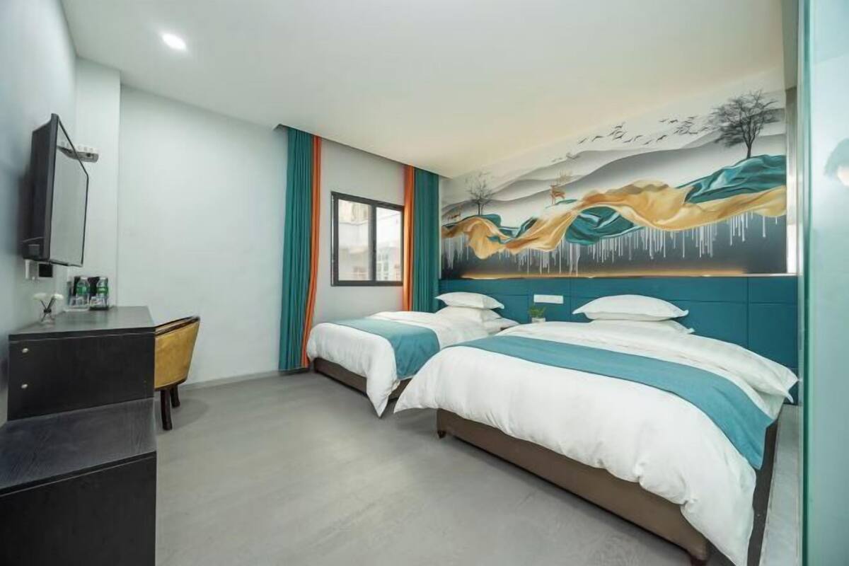 A hotel room with two beds, a desk, a TV, and a mural on the wall.