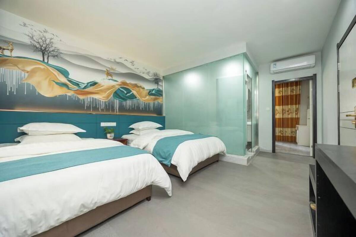 A hotel room with two beds, a mural on the wall, a TV, and an air conditioning unit.