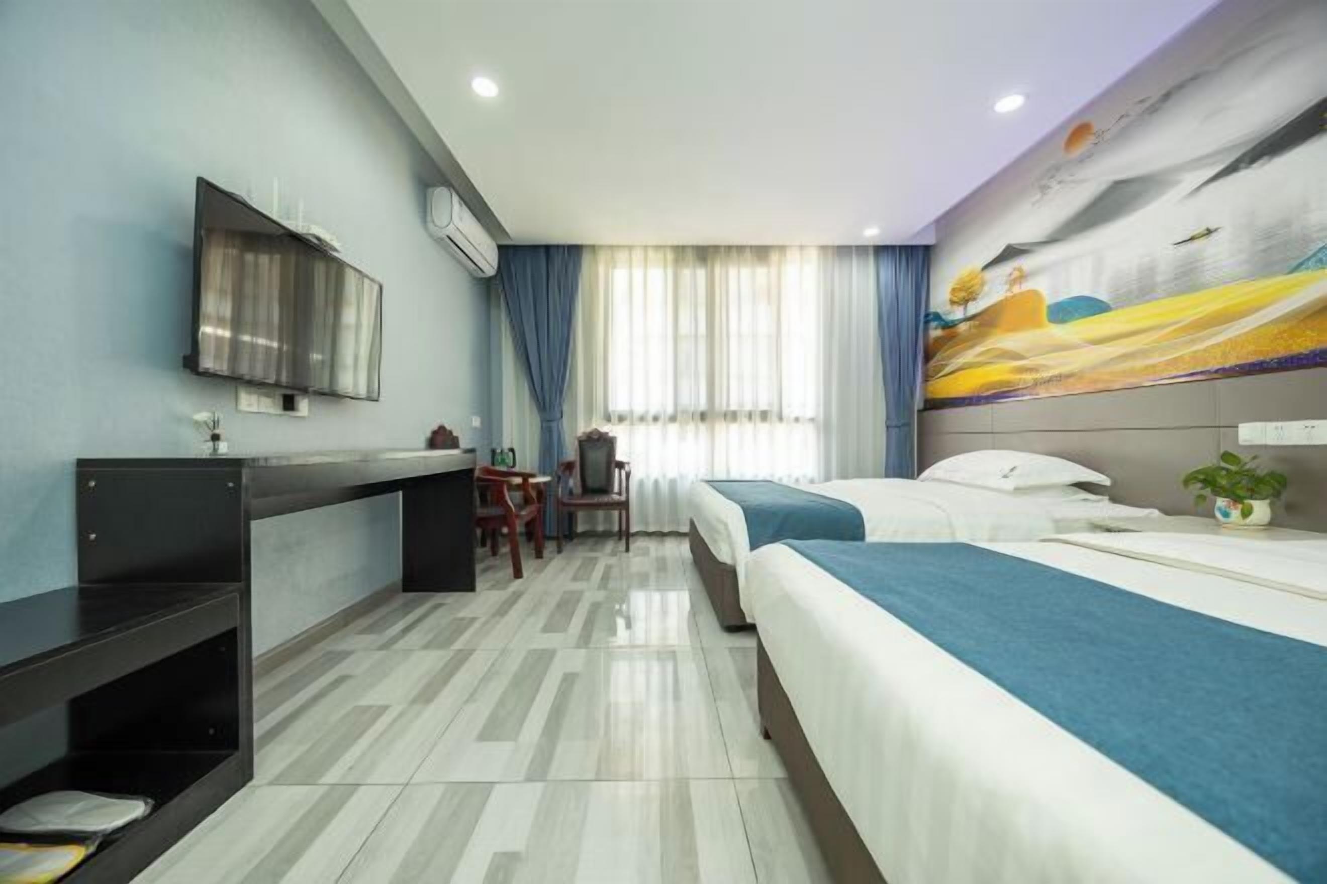 Habitación de hotel con dos camas, un escritorio, una silla, un televisor y un ventanal grande con cortinas.