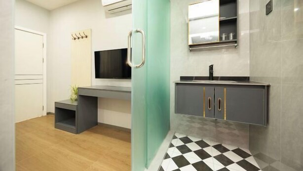 A modern bathroom with a grey vanity, a black sink, and a mirror above it. There is a small shelf with toiletries and a plant on the vanity. - Yinlilai Business Hotel (Tianquan Hospital of Traditional Chinese Medicine Branch) (Tianquan)