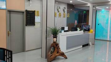A reception area with a reception desk, a wooden plant stand, a wall clock, and a digital screen.