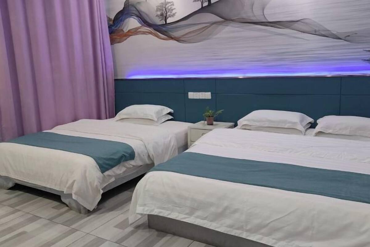 A hotel room with two beds, a large mural on the wall, and a nightstand with a plant.