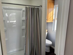 A bathroom with a shower curtain, a toilet, and a wooden cabinet. - Spacious waterfront home recently remodeled with WiFi, AC, and cable TV. (Oconto)