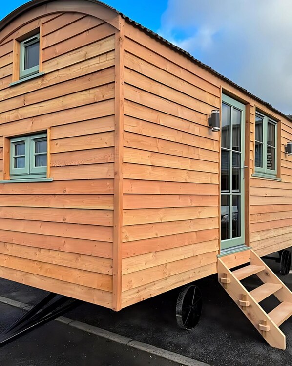 A wooden mobile home with a curved roof, a sliding door, and a small set of stairs leading to the entrance.
