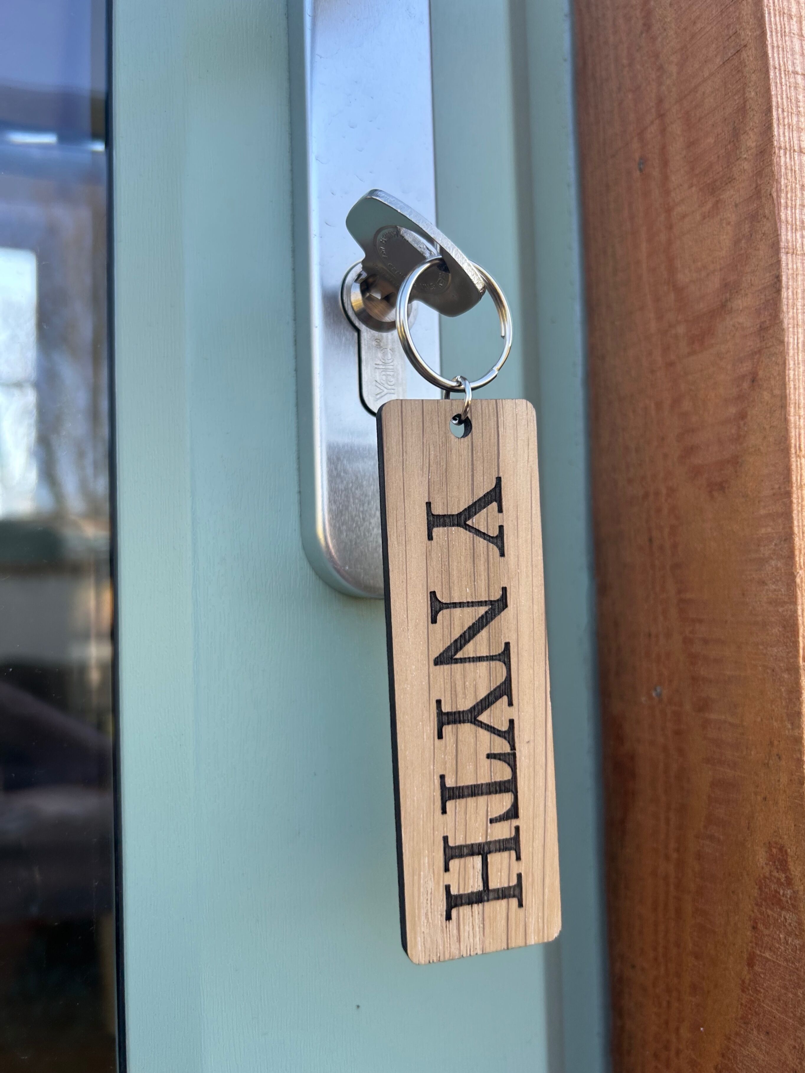 Een houten sleutelhanger met de naam 'HILAN' eraan bevestigd aan een deurklink.