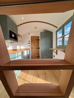 A modern kitchen with wooden cabinetry, a built-in oven, and a window overlooking a balcony.